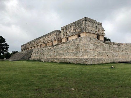 Gobernor Palace in Uxmal, Yucatan, Mexico with a cloudy sky and green grass with a tree at the back