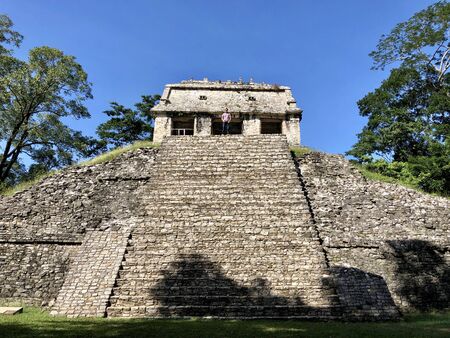 Templo del Conde in Palenque, Chiapas, Mexico with a guy on the top with some trees and a blue skyの写真素材