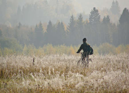 The bicyclist goes in the early autumn morning across the field of covered with hoarfrostの写真素材