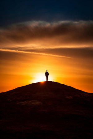 Silhouette of a man standing on top of a mountain and watching the sunsetの素材