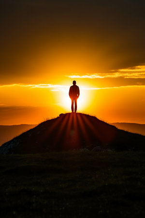 Silhouette of a man standing on the top of a mountain at sunsetの素材