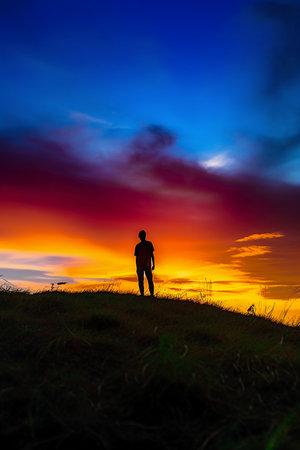 Silhouette of a man standing on the top of a hill at sunsetの素材