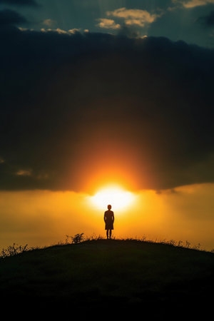 Silhouette of a man standing on the top of the hill and looking at the sunsetの素材