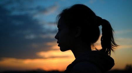 Silhouette of a girl with long hair against the setting sunの素材