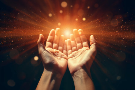 Close up of human hands gesturing against dark background with light raysの素材