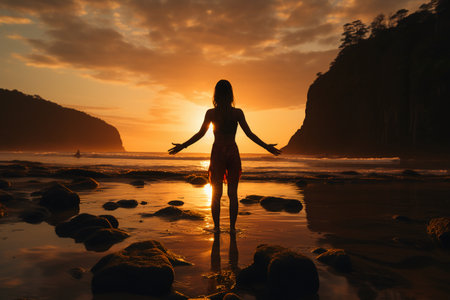 Silhouette of a young woman standing on the beach at sunsetの素材