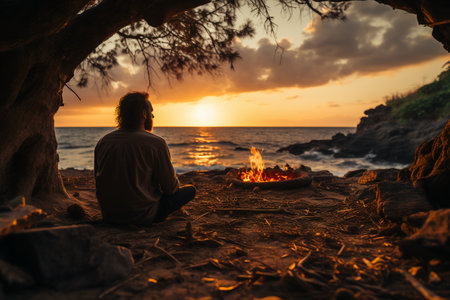 Man sitting on the beach in front of a campfire at sunsetの素材