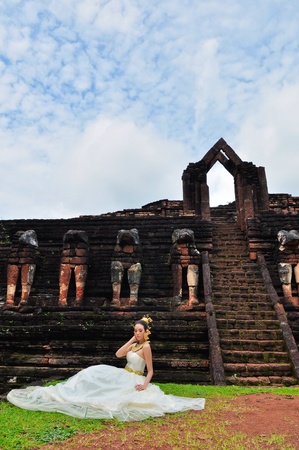 Beautiful woman in Thai traditional dress sitting in front of ancient monumentの写真素材