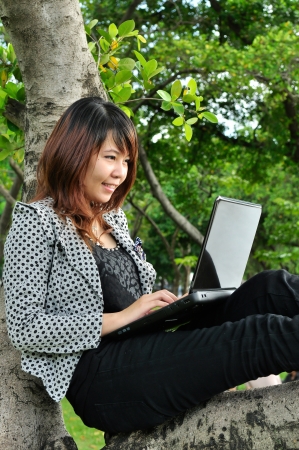 Portrait of beautiful woman smiling on the tree and playing laptopの写真素材
