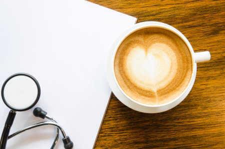 A cup of coffee with heart shape, Stethoscope and open blank book on grungy wood backgroundの写真素材