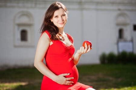 Beautiful pregnant woman sitting outdoor with red appleの写真素材