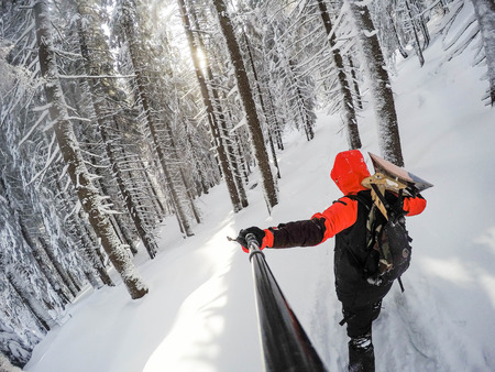 Man with snowboard up the snowy woods on a mountain topの写真素材