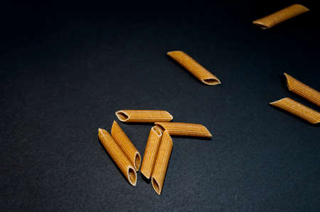 A group of Italian pasta on black background. Penne rigate type of macaroni which are uncooked and made from whole grain.の写真素材