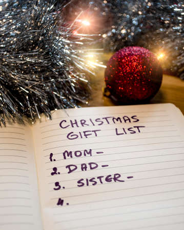 Christmas gift list and some shiny holiday decorations. An English inscription in the notebook "Christmas gift list - mom, dad, sister".の写真素材