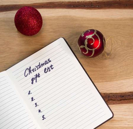 Minimal Christmas decorations on retro oak wood table and a handwritten gift list on lined paper. An English text handwritten in a paper notebook "Christmas gift list".の写真素材