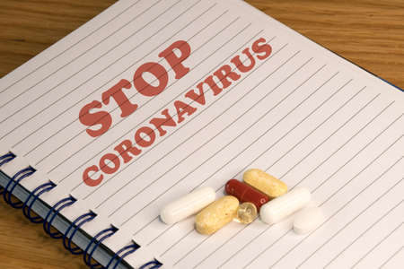 Notebook with English text "Stop coronavirus". Colorful pills and capsules are vitamins to support the immune system. Selective focus on the text, blurred background and the medicine.の写真素材