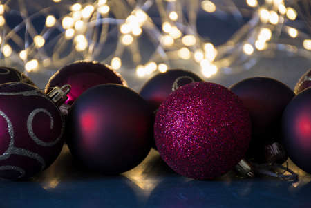 Festive concept of Christmas decorations. Dark red shiny baubles on black background, Christmas tree lights illuminating the background of decorations. Selective focus on balls, blurred background.の写真素材