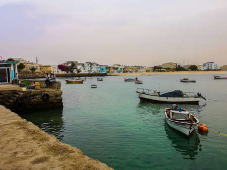 Sal Rei, Cape Verde - February 10th 2019: green water of the bay and small fishing boats floating in the marine. African fishermen chilling on the shore.のeditorial素材