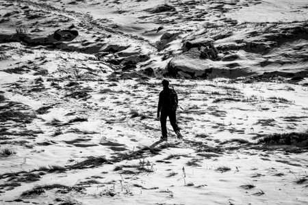 One man hiking in High Tatras, Poland. Lonely tourist in the valley during cold winter time. Withered grass hiding under the snow. Selective focus on the person, blurred background.の写真素材