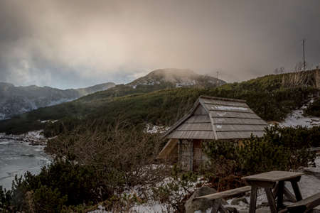 Clouds rising over Tatra Mountain valley and covering the peaks. Old wooden chalet and benches are abandoned. Selective focus on the bushes, blurred background.の写真素材