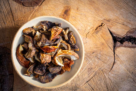 Dried boletus mushrooms in a ceramic bowl on a piece of natural wood. Organic freshly sliced forest harvest. Selective focus on food, blurred background.の写真素材