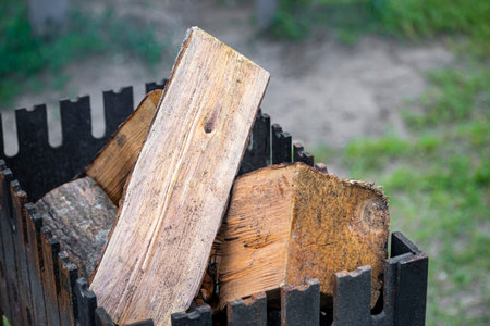 Deciduous tree logs in a fireplace. Black rusty grill, outdoor camping and grilling in a park,...