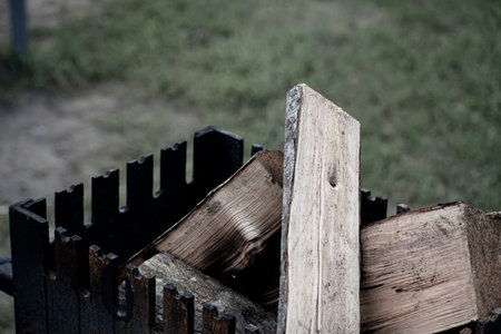 Dry wood logs in rustic fireplace. Black metal grill with firewood inside. Grilling and camping in a park. Summertime picnic. Selective focus on the texture of the wood, blurred background.の写真素材