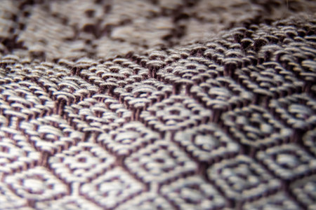 Brown and white handmade material closeup. Macro photography of woven cotton cloth with white and brown ornaments. Selective focus on the threads, blurred background.の写真素材