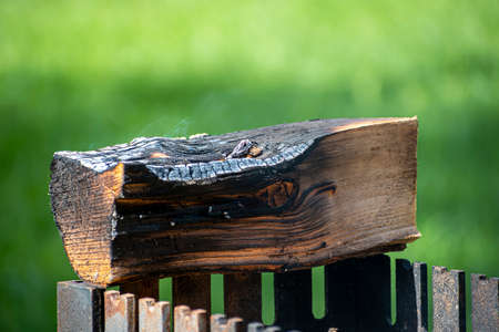 Smoking piece of wood on metal grill. Green lawn in Valakampiai Park, Vilnius, Lithuania. Public outdoor fireplace for grilling and picnic. Selective focus on the details, blurred background.の写真素材