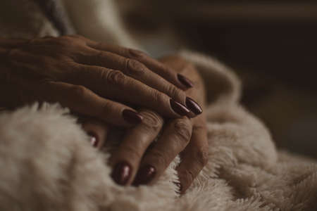 Elegant nail design for a woman. Neat manicure, dark red royal color gel polish, cozy home concept. Selective focus on the details, blurred background.の写真素材