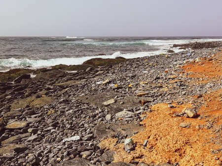 Large rocks on the shore of the ocean. Rough and stormy sea, black stones and bright orange sand on the coastline. Selective focus on the details, blurred background.の写真素材