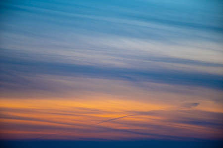 Bright sunset sky with clouds. Orange and blue vibrant colors, winter evening sky pattern, dramatic cloudscape. Selective focus on the details, blurred background.の写真素材