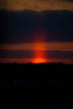 Orange light pillar closeup. Dark evening sky in winter. Atmospheric phenomenon with sunlight ice crystals in cold air. Selective focus on the details, blurred background.の写真素材