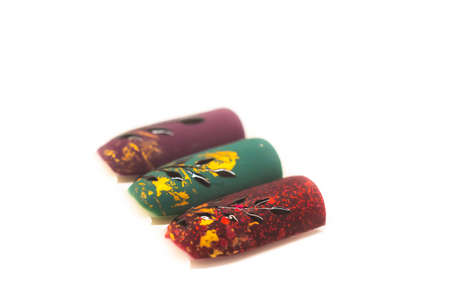 Matte nail design on tips. Red, green and bordeaux gel polish with golden aluminium foil and black painted floral elements. Selective focus on the details, object isolated on white background.の写真素材