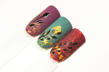 Festive nail designs on white background. Matte colorful gel polish with black shiny paint and golden foil. Selective focus on the details, blurred background.の写真素材