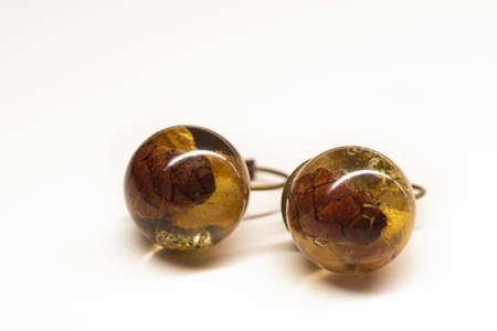 Sphere resin ball earrings closeup. Natural dried plants inside handmade jewelry. Smooth surface, brass base. Selective focus on the details, object isolated on white background.の写真素材