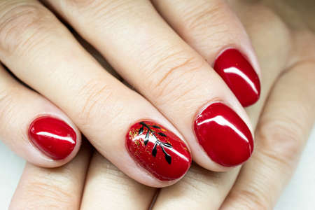 Red gel polish on female fingernails. Painted black floral decorations, golden foil, neat manicure. Selective focus on the details, blurred background.の写真素材