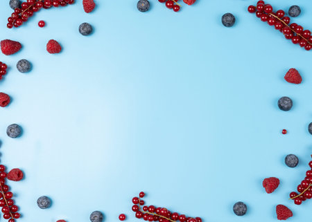 Mixed berries on a blue background, scattered blueberries and raspberries and red currants frame for design with copy spaceの写真素材