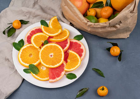 Fresh sliced citrus fruits on a plate. Orange, grapefruit, lemon, lime, tangerine on a gray table. Assorted fresh citrus fruits with leaves. Top viewの写真素材