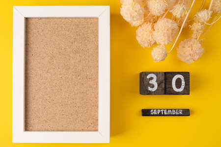 Mockup white picture frame, dry flower with wooden calendar. 30 September date on wooden calendar on a yellow background with dry flowersの写真素材