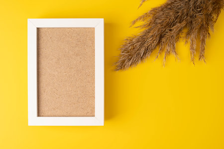 An empty wooden photo frame lies on a yellow background, fluffy branches, dried flowers. Idea - wooden frame mockup, autumn photo frameの写真素材