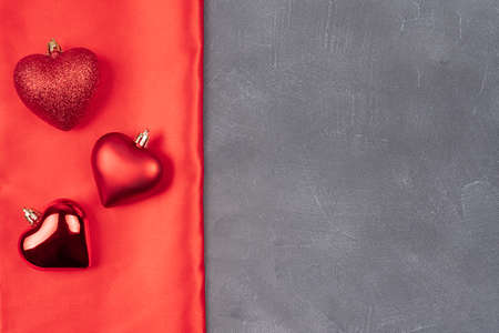 Valentines day flat lay copy space. On a gray background and a red bow, red ball hearts, hearts made of ball shape of a heart, red satin texture. Christmas conceptの写真素材