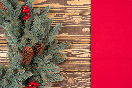 Decorative Christmas wreath with pine cone on natural wooden table background with red tablecloth borderの写真素材