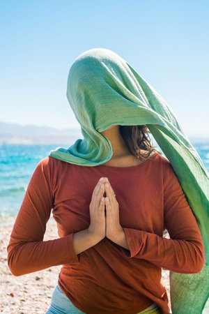 Portrait of young woman with long green scarf on head on the beach with sea backgroundの写真素材