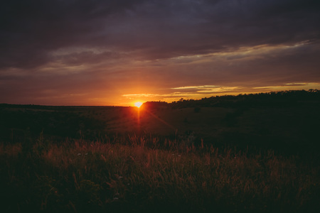 Sun sets over the tops of forest trees in clouds. Panoramic photo of purple, orange and dark clouds in the sky illuminated by the setting sunの写真素材