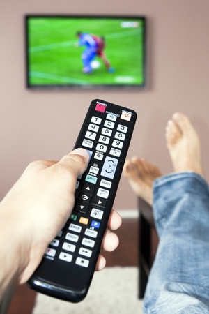 Young man watching the television, the remote control in hand.の写真素材