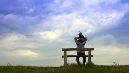 The man sits on a bench under a cloudy sky 
