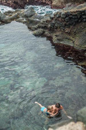 Father and daughter swimming in the natural swimming pool Charco De La Laja, at the north of Tenerife, Canary Islands, Spainの写真素材