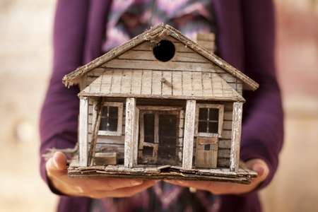 Woman holding old minature house that is falling apart. の写真素材