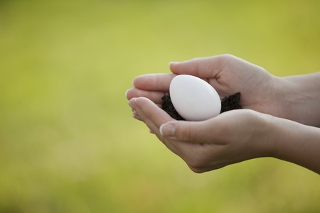 A woman gently holds an egg and dirt in her hands  の写真素材